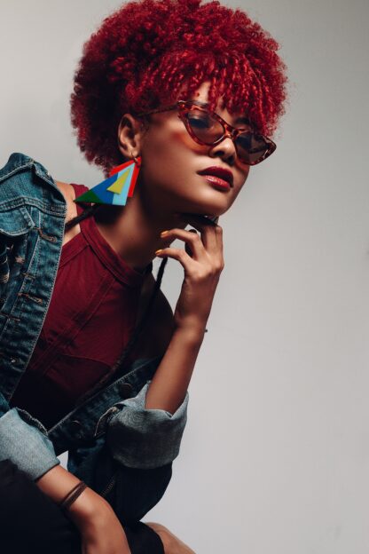 Beautiful woman wearing denim jacket and large statement jewellery and sunglasses, with natural hair dyed red