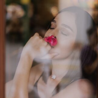 Blurred image of beautiful woman with beautiful skin, wearing sleeveless top, viewed through a glass screen or window, eyes closed and holding a rose to her face