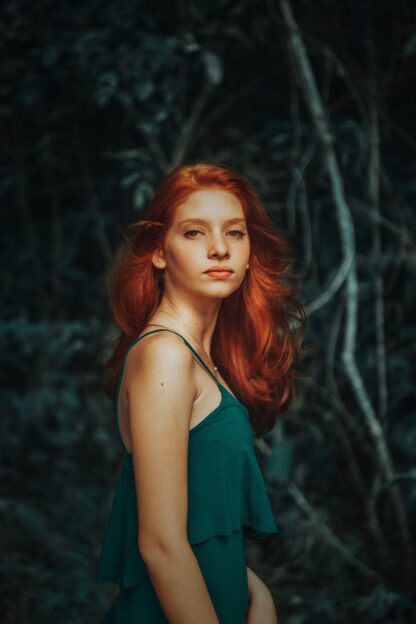woman with long ginger hair wearing a strappy green dressagainst a natural green background