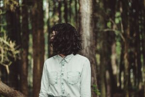 organic hair colour; woman with short black hair covering her face, forest scene.