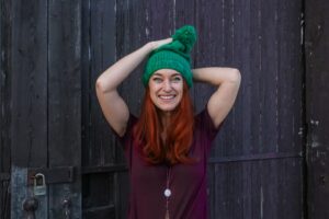 young smiling woman wearing a green beanie hat over long deep auburn hair coloured with herbal hair dye organic and natural hair colour