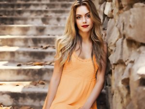 Organic hair conditioner rhubarb root powder, woman with long healthy blonde hair in ornage dress standing against a stone wall and steps