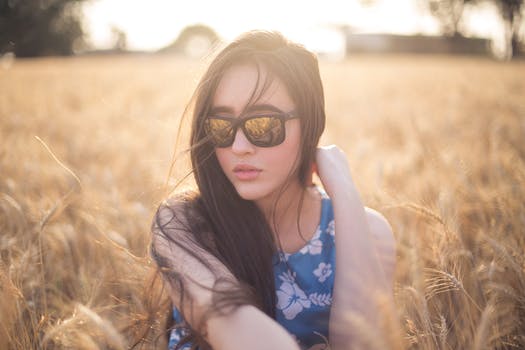 Young woman in sunglasses with long brown hair swept over one shoulder, in a sleeveless patterned blue dress . Shikakai hair wash is especially good for fine, fly away hair