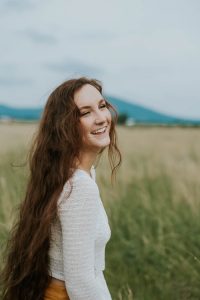 Argan oil for natural hair health, a natural hair conditioner; photo of smiling young woman with long brown hair down her back, standing in a field,