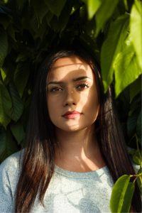 Best chemical free hair dye image of young woman with straight long brown hair standing under the shade of a leafy tree