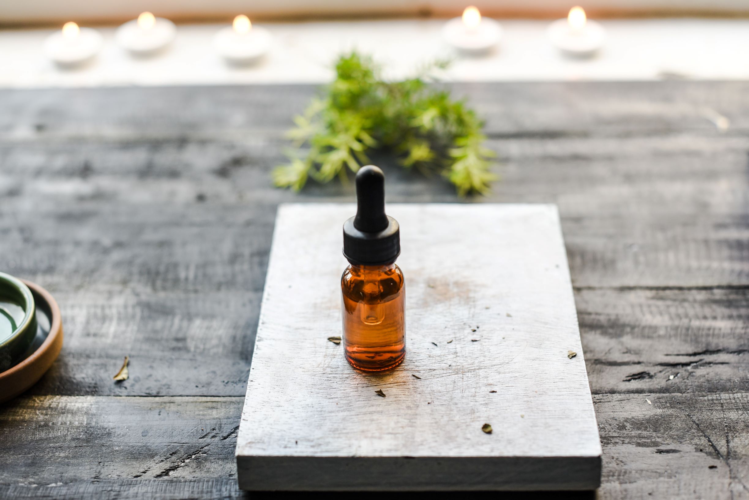 photo of brown opaque dropper bottle with black lid placed on a small rectangular slab of wood, outdoors, depicting amla hair care