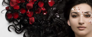 Close up image of beautiful Mediterranean looking woman with long black wavy hair with red rose petals  in it
