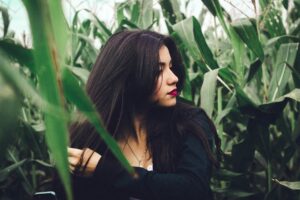 Natural hair dyes without chemicals picture of woman with straight , shoulder length, black hair ,wearing white T-shirt type top under black jacket as she's walking through tall green crops. 